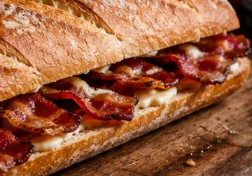 Crusty bacon baguette filled with crisp bacon and melted cheese on a wooden board
