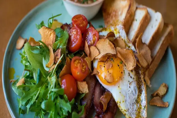 Fried egg, bacon, cherry tomatoes, salad leaves and toast on a blue plate