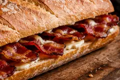 Crusty bacon baguette filled with crisp bacon and melted cheese on a wooden board