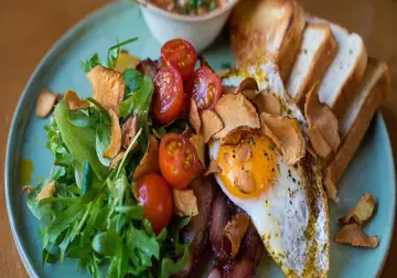 Fried egg, bacon, cherry tomatoes, salad leaves and toast on a blue plate