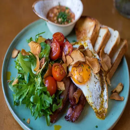 Fried egg, bacon, cherry tomatoes, salad leaves and toast on a blue plate
