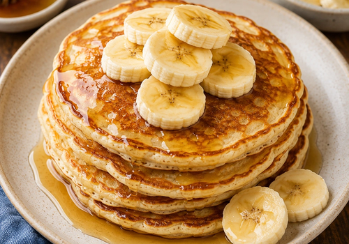 Stack of golden banana pancakes topped with banana slices and drizzled with honey