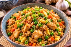 Chicken fried rice with egg, peas, carrots and spring onions in a ceramic bowl
