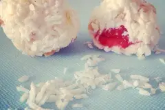 Two coconut-coated chocolate yoghurt balls, one cut open to show a strawberry centre