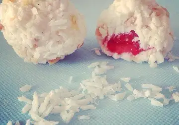 Two coconut-coated chocolate yoghurt balls, one cut open to show a strawberry centre