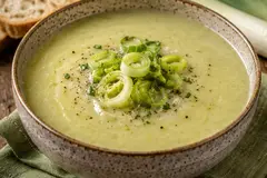 Creamy leek and potato soup in a ceramic bowl topped with sliced leeks and black pepper