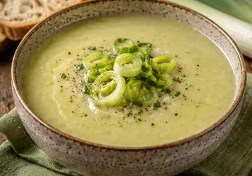 Creamy leek and potato soup in a ceramic bowl topped with sliced leeks and black pepper