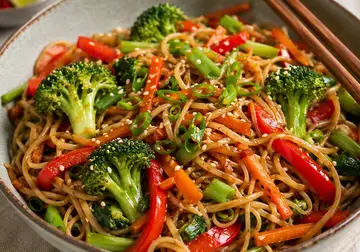 Bowl of sweet chilli noodles with broccoli, red pepper, carrot, spring onion and sesame seeds