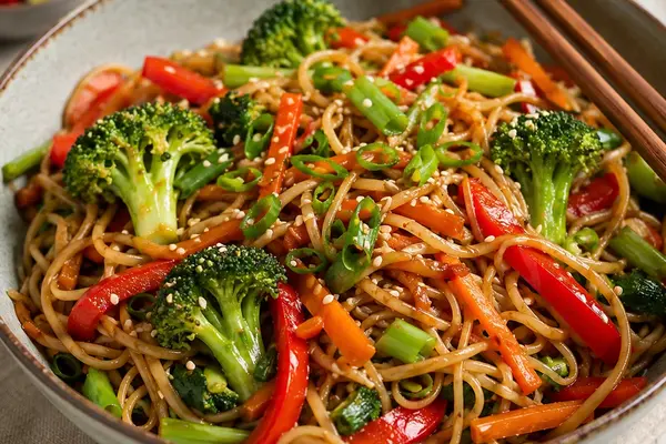 Bowl of sweet chilli noodles with broccoli, red pepper, carrot, spring onion and sesame seeds